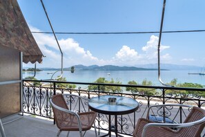 A balcony with wicker chairs and a glass table overlooking a body of water with boats and mountains in the distance. - Room 'Double  Sea View 7' with Sea View, Wi-Fi and Air Conditioning (Nikiana)