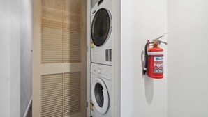Une buanderie équipée d’un lave-linge et d’un sèche-linge à chargement frontal, d’un extincteur fixé au mur et d’une porte à ventilation.