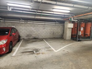 A parking garage with a red car parked in a reserved space, concrete walls, and industrial pipes. - Cityscape on White - Auckland Central Studio (Auckland)