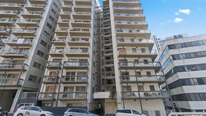 Un immeuble résidentiel à plusieurs étages, doté de balcons, d’une entrée principale et d’un espace de stationnement avec des voitures.