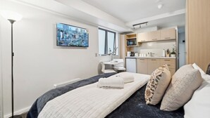 Une chambre d’hôtel moderne équipée d’un lit, d’un bureau, d’une chaise, d’une kitchenette et d’une grande fenêtre.