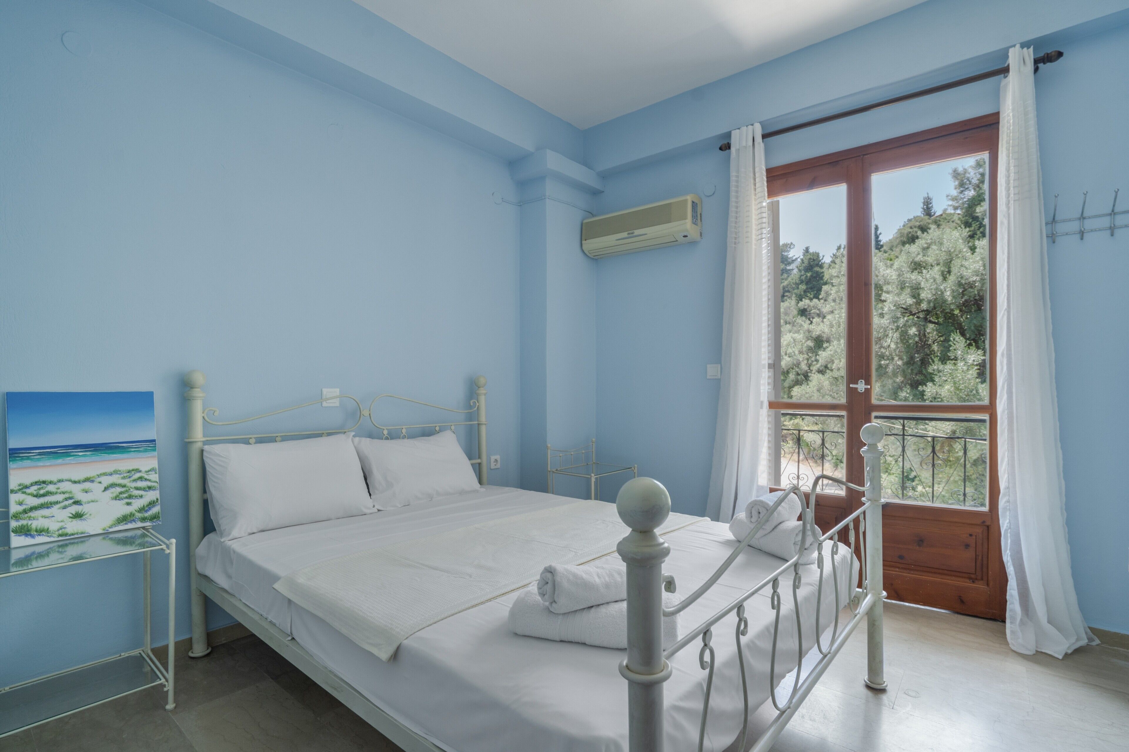 Un dormitorio con cama, ventana con cortinas, un cuadro en la pared y puerta al balcón.