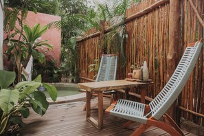 A wooden deck with a table and two chairs, surrounded by lush greenery and a bamboo fence. - LUúM, A WELL-LOCATED OASIS, IDEAL FOR RECONNECTING WITH NATURE. (Mérida)