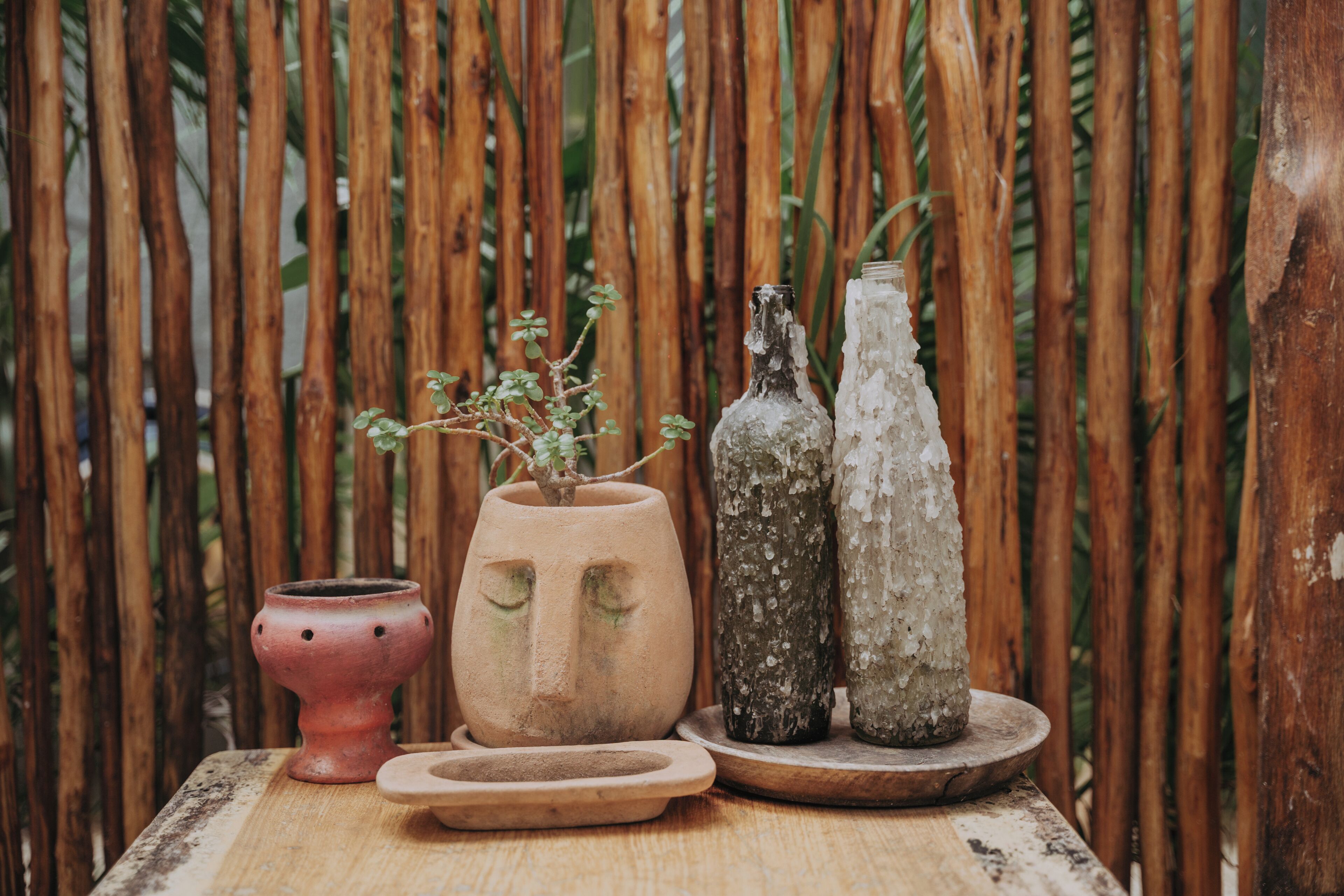 Une table en bois rustique, agrémentée de trois pots en céramique et de deux bouteilles, le tout placé devant un décor de bambous.