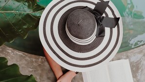 Henkilö rentoutuu uima-altaan äärellä, kädessään kirja ja juomaa, ja häntä ympäröivät suuret vihreät lehdet sekä kelluvat ruusun terälehdet.