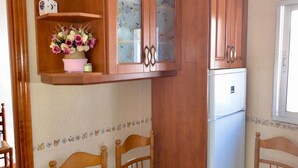 A compact kitchen with wooden cabinets, a refrigerator, and two wooden chairs. - Brother's Village (Villardefrades)