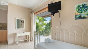 A bedroom with a bed, a desk, a television, and a balcony with a view of greenery.