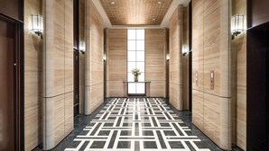 Un hall d’ascenseur moderne avec un sol à motifs géométriques, des murs en bois et un luminaire central.