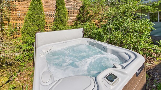A hot tub with a digital control panel, surrounded by greenery and a building in the background.