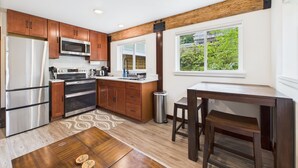 A modern kitchen with wooden cabinets, stainless steel appliances, and a large window offering a view of greenery.