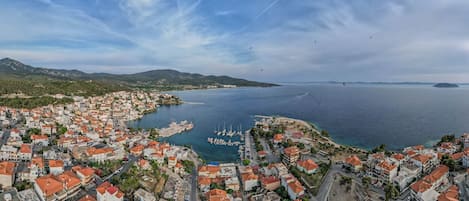 A coastal town with a marina, red-roofed buildings, and a clear view of the sea and distant islands.