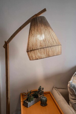 A floor lamp with a woven shade, a wooden side table with a plant and a decorative item, and a beige sofa.