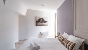 A modern hotel room with a large bed, a painting on the wall, and a window providing natural light.