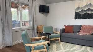 Un salon avec un canapé gris, des fauteuils turquoise, une petite table noire et un tapis vert à motifs.