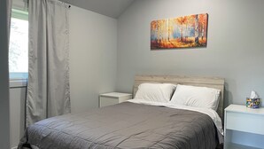 Une chambre à coucher avec un lit, une table de chevet, un tableau au mur et une fenêtre avec des rideaux.