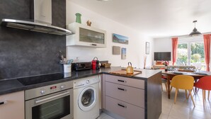 Eine moderne Küche mit Einbauofen, Mikrowelle und Waschmaschine. Es gibt eine Essecke mit Tisch und Stühlen sowie ein großes Fenster mit Vorhängen.