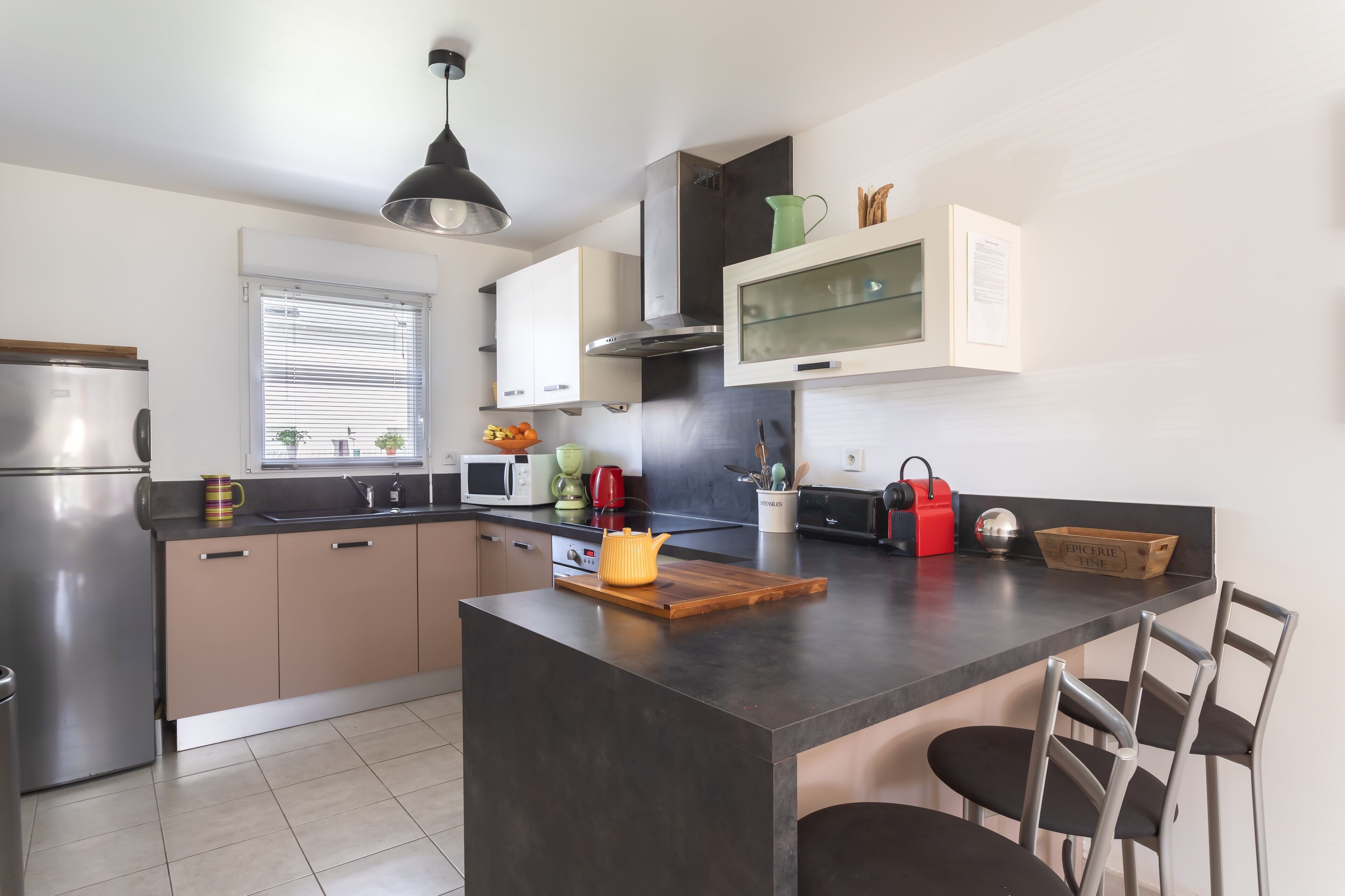 A modern kitchen with a central island, stainless steel appliances, and a window with blinds.