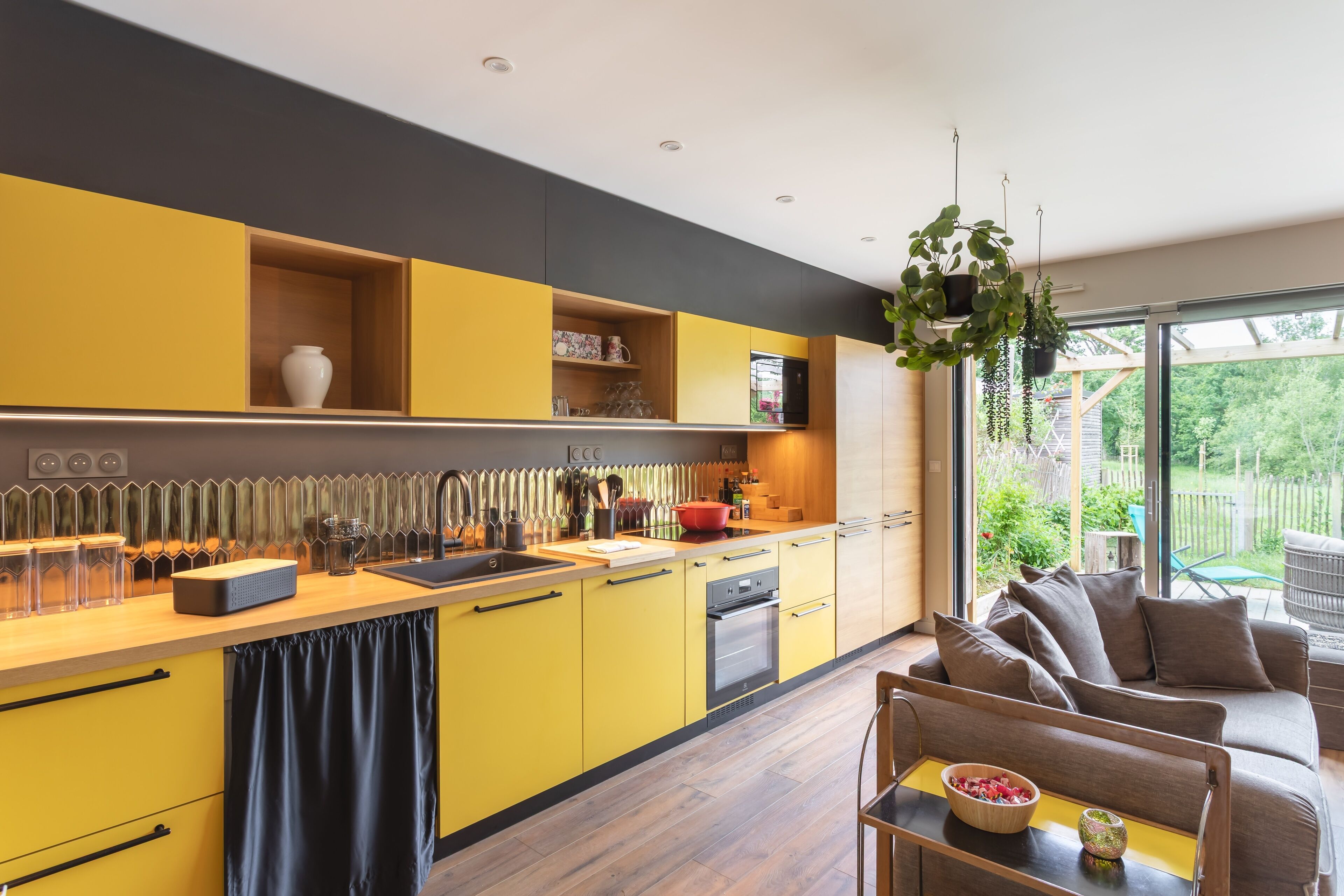Une cuisine moderne avec des armoires jaunes, un plan de travail en bois et un four encastré. On y trouve également un coin repas avec un canapé et une table.