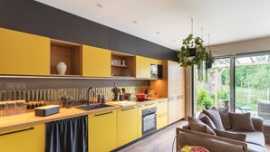 A modern kitchen with yellow cabinets, a wooden countertop, and a built-in oven. There is a dining area with a sofa and a table. - La Petite Mare - proche de Rennes (Saint-Jacques-de-la-Lande)