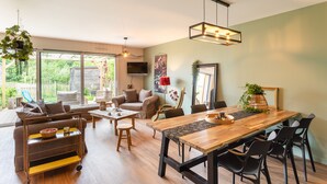 A spacious living area with a wooden dining table, black chairs, a sofa, and a TV. - La Petite Mare - proche de Rennes (Saint-Jacques-de-la-Lande)