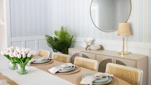 A dining area with striped wallpaper, a round mirror, a table set with plates and napkins, a plant, and a lamp.