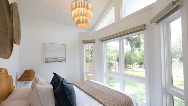 A bedroom with a large bed, a chandelier, a view of the outdoors, and a framed picture on the wall.