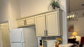 A kitchen with white cabinets, a white refrigerator, a wooden island with bar stools, and a hanging light fixture. - Charming 3-bdrm house w/ community pool + clay tennis courts in Melbourne Beach (Melbourne Beach)