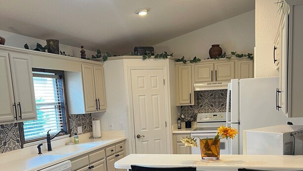 A modern kitchen with white cabinetry, a central island with bar stools, a built-in oven, and a refrigerator. - Charming 3-bdrm house w/ community pool + clay tennis courts in Melbourne Beach (Melbourne Beach)