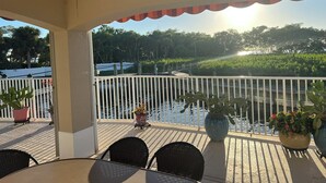 A covered outdoor area with a table and chairs, a ceiling fan, and a view of a water body and greenery. - Charming 3-bdrm house w/ community pool + clay tennis courts in Melbourne Beach (Melbourne Beach)
