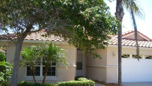 A single-story house with a tiled roof, a garage, and a well-maintained lawn with trees and shrubs. - Charming 3-bdrm house w/ community pool + clay tennis courts in Melbourne Beach (Melbourne Beach)