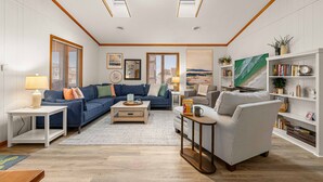 A spacious living room with a sectional sofa, a striped armchair, a coffee table, and a bookshelf. - Steps to Beach - Playroom - Firepit - Pets OK (Kill Devil Hills)