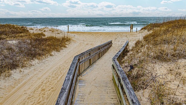 A wooden boardwalk leading to the beach with sand and sparse vegetation on either side. - Steps to Beach - Playroom - Firepit - Pets OK (Kill Devil Hills)