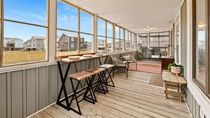 A covered outdoor deck with wooden benches and tables, large windows, and a view of neighboring houses. - Steps to Beach - Playroom - Firepit - Pets OK (Kill Devil Hills)