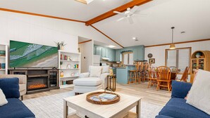 A spacious living room with a fireplace, a television, and a dining area with wooden chairs and a table. - Steps to Beach - Playroom - Firepit - Pets OK (Kill Devil Hills)