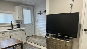 Kompakti keittiö, jossa on valkoiset kaapit, puinen pöytä ja litteänäyttöinen televisio, joka on sijoitettu kaapin päälle.