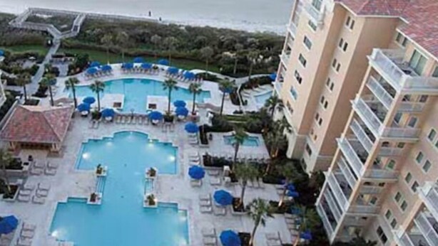 A resort with a central pool surrounded by lounge chairs and umbrellas, adjacent to a beachfront hotel. - Oceanfront Charming 2-bedroom hotel in delightful Myrtle Beach (Myrtle Beach)