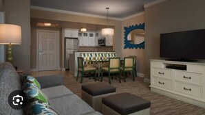 A compact living space with a sofa, ottoman, dining table with chairs, a kitchen area, and a television on a cabinet. - Oceanfront Charming 2-bedroom hotel in delightful Myrtle Beach (Myrtle Beach)