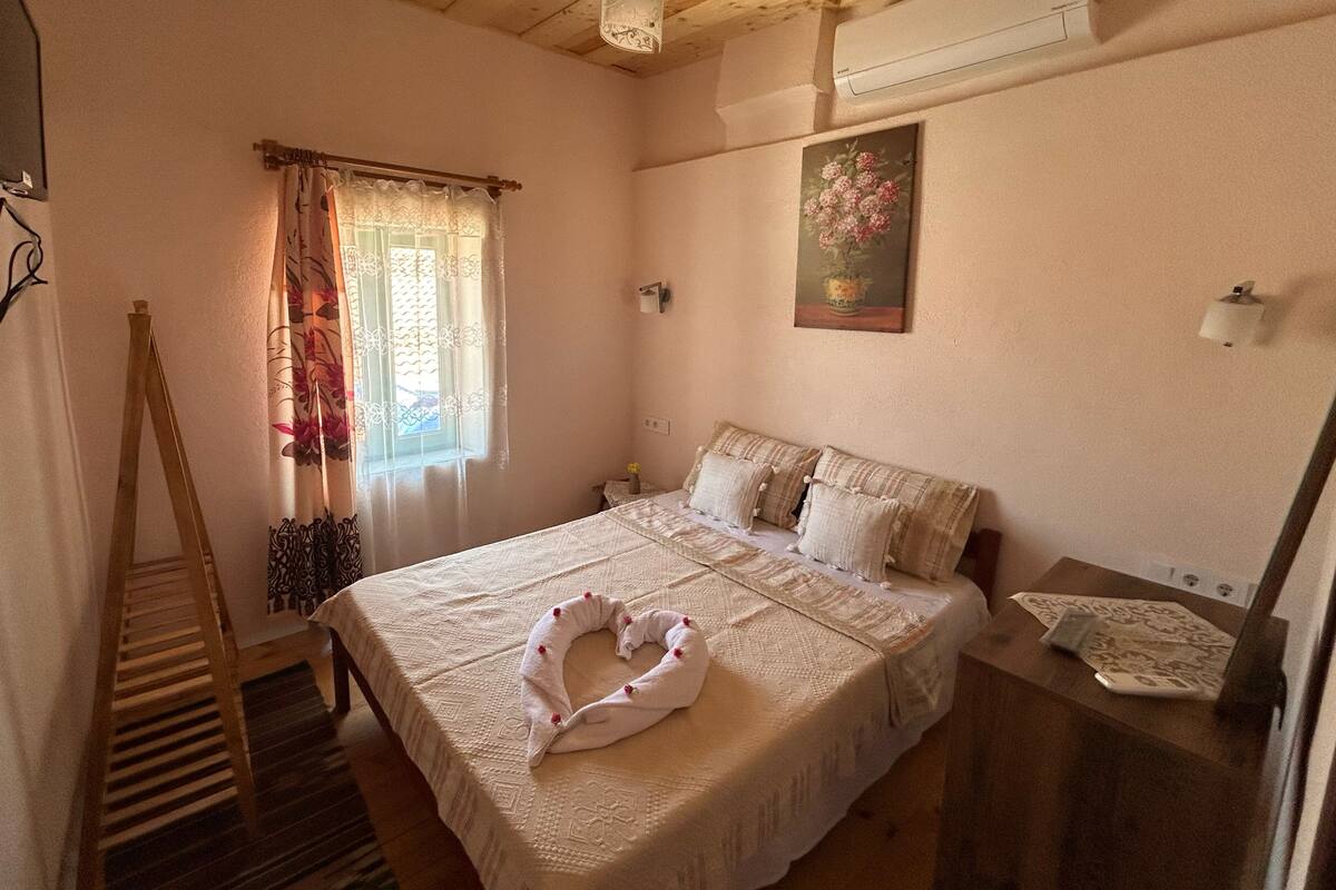 A bedroom with a bed, a wooden ladder, a window with curtains, a wall-mounted light, and a painting.