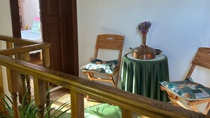 Una habitación con una escalera de madera, dos sillas de madera con cojines estampados, una mesita redonda con mantel verde y una planta en maceta.