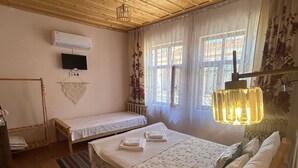 Una habitación acogedora con techos y paredes de madera, una cama con ropa de cama estampada, una mesita de noche pequeña, un televisor montado en la pared y una ventana con cortinas.