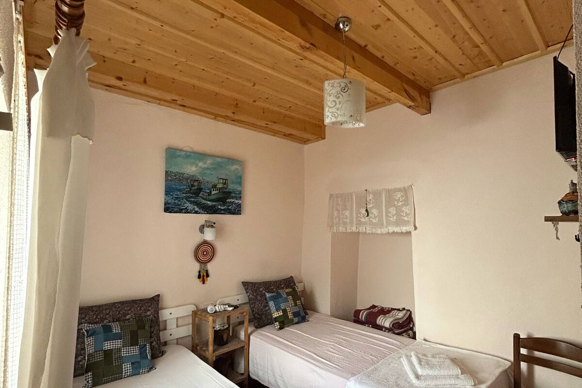 A room with two beds, wooden ceiling beams, a painting on the wall, and a hanging light fixture.