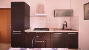 A compact kitchen with dark cabinets, a gas stove, a sink, and a white backsplash. - Porticciolo 3 vista mare x 4 persone (Viserba)