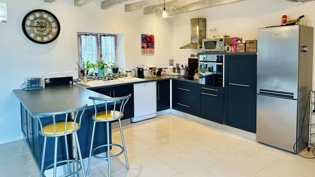 Una cocina moderna con armarios oscuros, un refrigerador de acero inoxidable y una barra con taburetes.