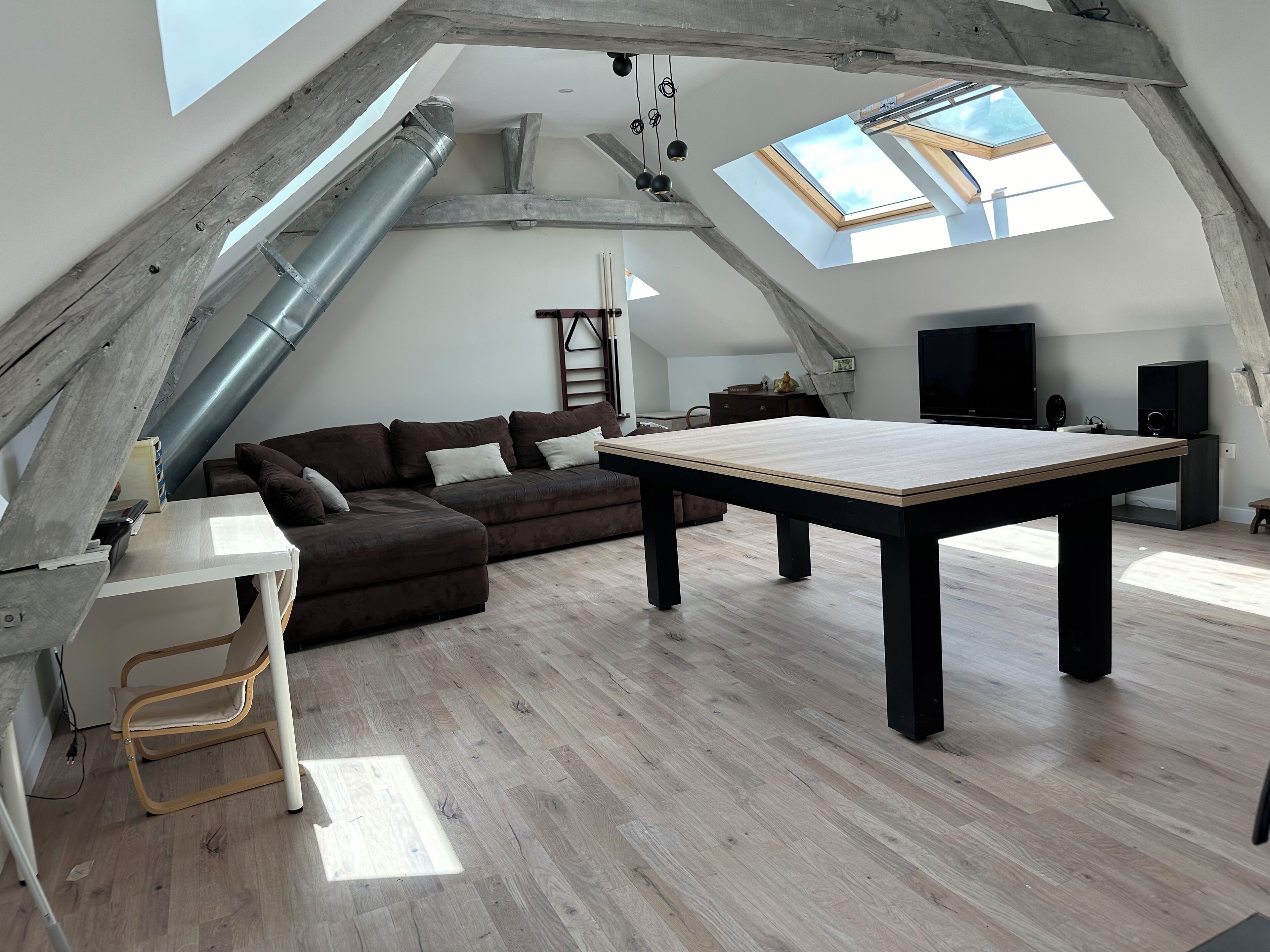 A loft-style room with a sloped ceiling, a wooden table, a sofa, and a TV.