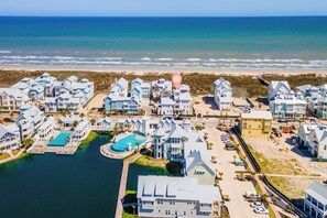 A coastal residential area with multiple houses, a swimming pool, and a beach in the background. - Once Upon a Beach 204 COA (Port Aransas)