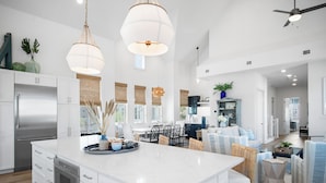 A spacious kitchen with white cabinetry, a large island, and modern pendant lighting. - Once Upon a Beach 204 COA (Port Aransas)