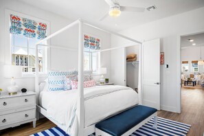A four-poster bed with a bench, white walls, and a view of a house through a window. - Once Upon a Beach 204 COA (Port Aransas)