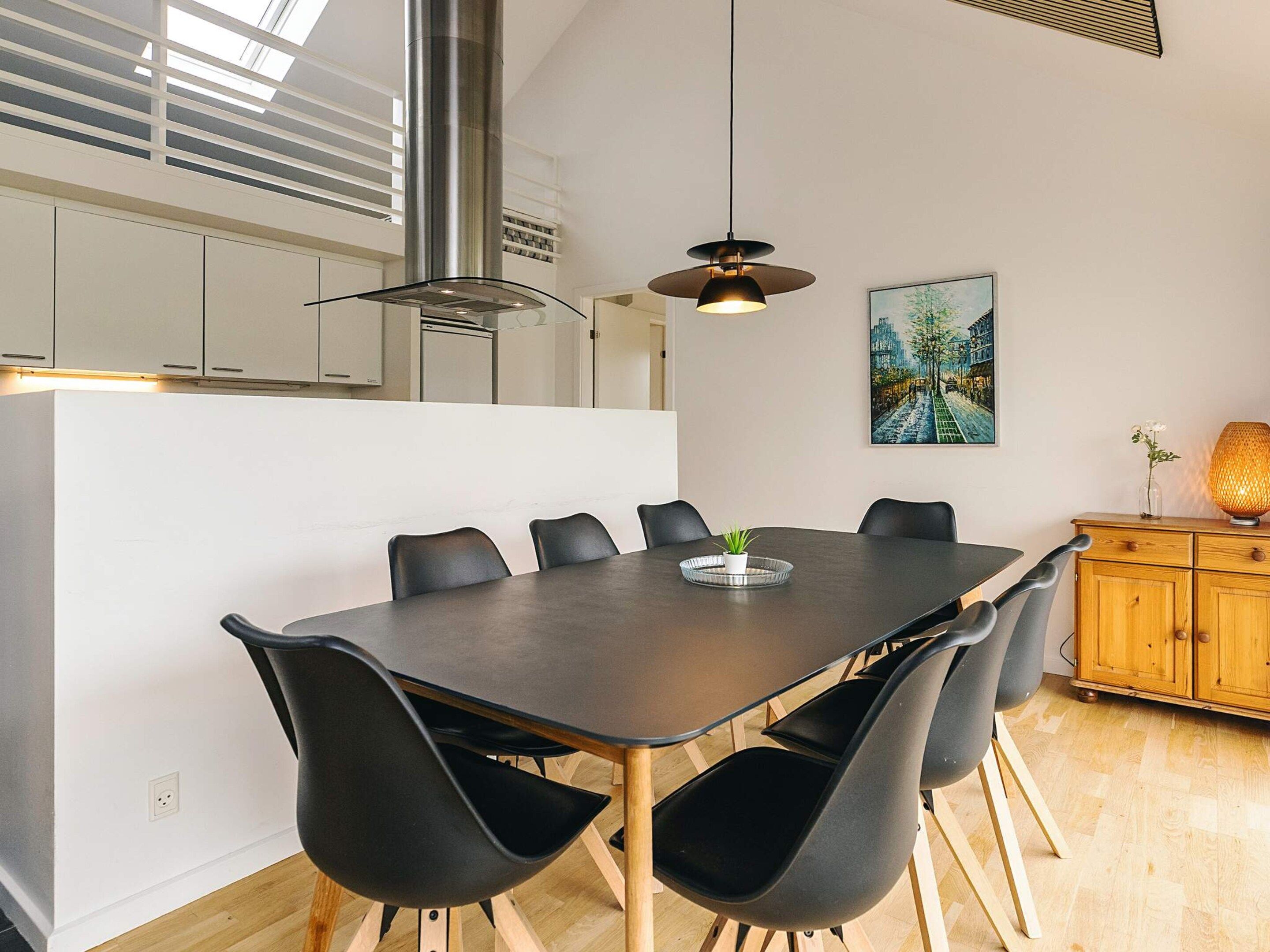 Uma cozinha moderna com uma mesa de jantar, cadeiras, uma luminária pendente e um quadro na parede.