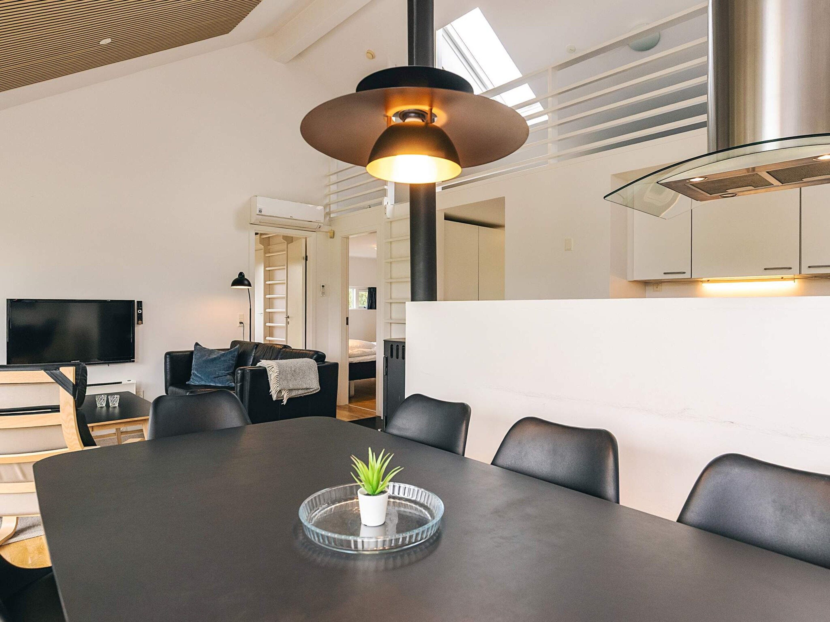 Un salon moderne avec une table à manger, des fauteuils en cuir noir, un téléviseur et une grande fenêtre.