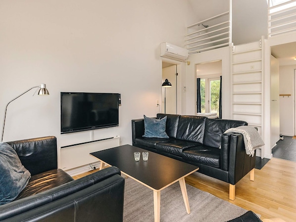A modern living room with a black leather sofa, a black coffee table, and a flat-screen TV mounted on the wall.